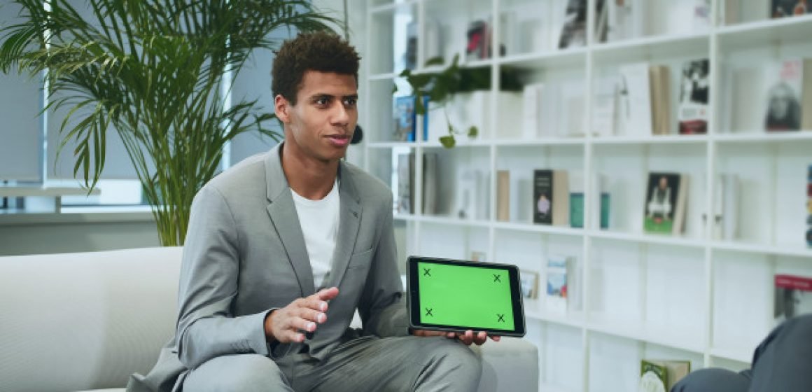 black-formal-man-making-presentation-with-tablet-with-green-chromakey-screen-young-african-american-man-suit-sitting-office-sofa-with-anonymous-colleague-making-presentation-with-tablet_178151-7